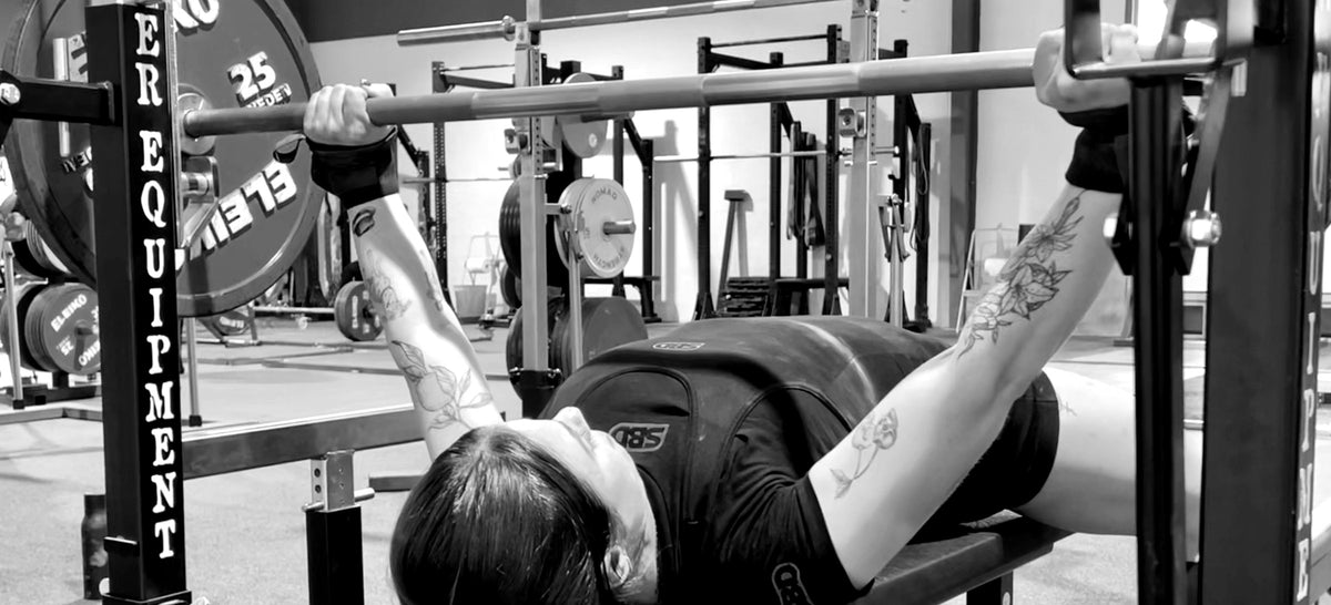 Woman bench pressing a loaded barbell at Desert Barbell strength gym in Dubai